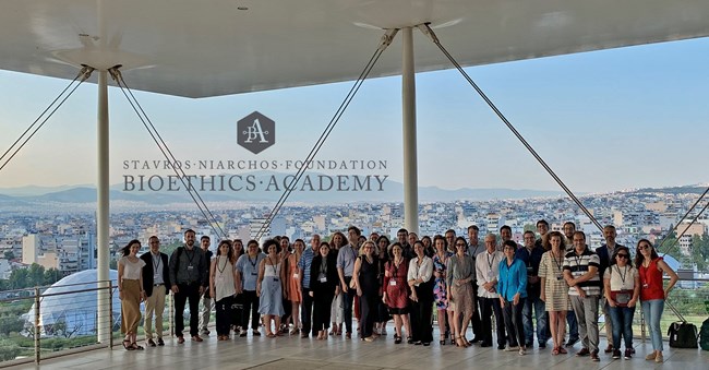 A large group poses for a photo at the Stavros Niarchos Foundation Cultural Center, overlooking Athens