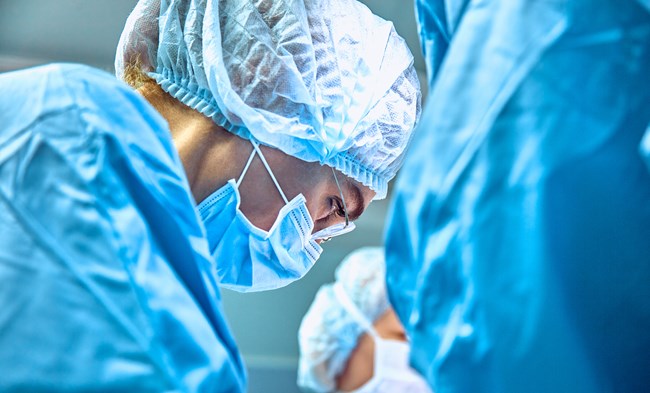 A medical professional wearing a surgical mask and hairnet focuses intently on a task