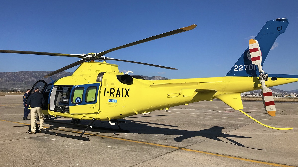 A person stands by the open door of a yellow and blue medevac helicopter with the SNF logo on it as it sits on the tarmac