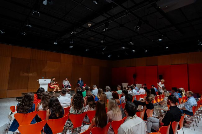 Seated audience attending a panel of three people in a large room.